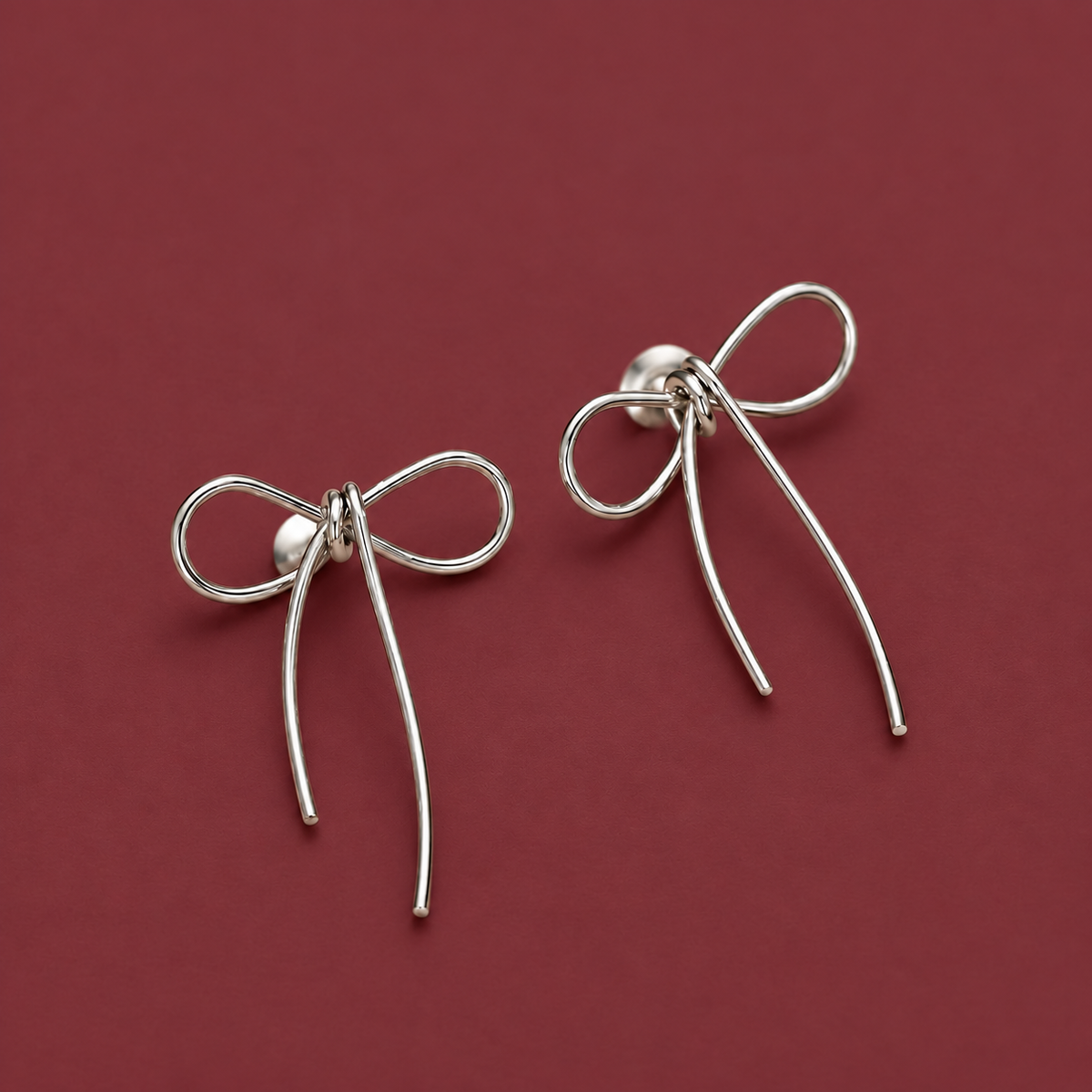 Gold-Tone Bow Studs — muted burgundy background