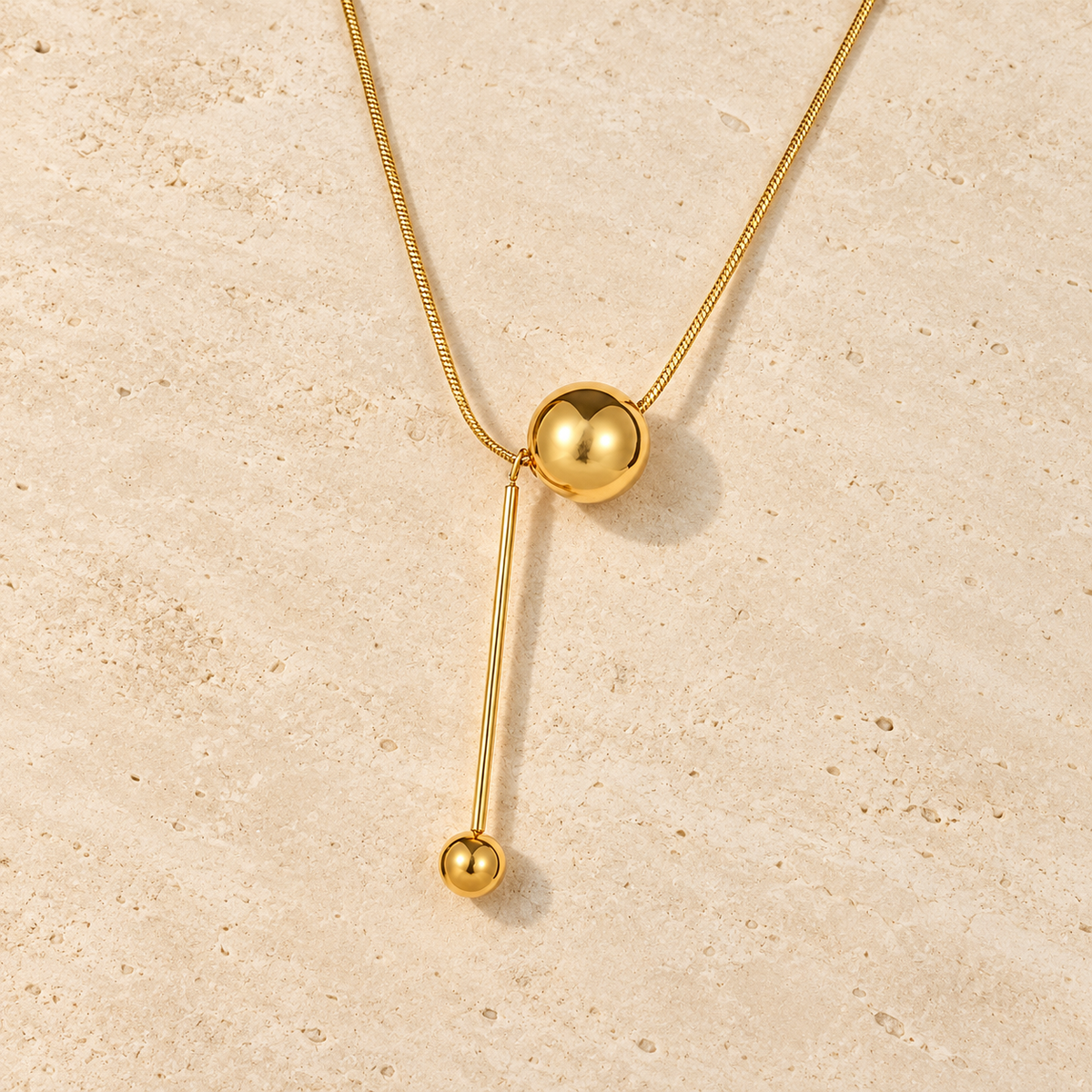 Gold Ball Y Necklace — pale beige natural stone background