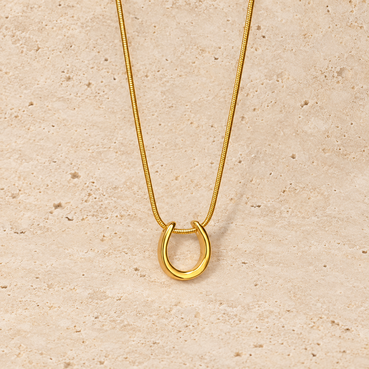 Gold Horseshoe Necklace — pale beige natural stone background