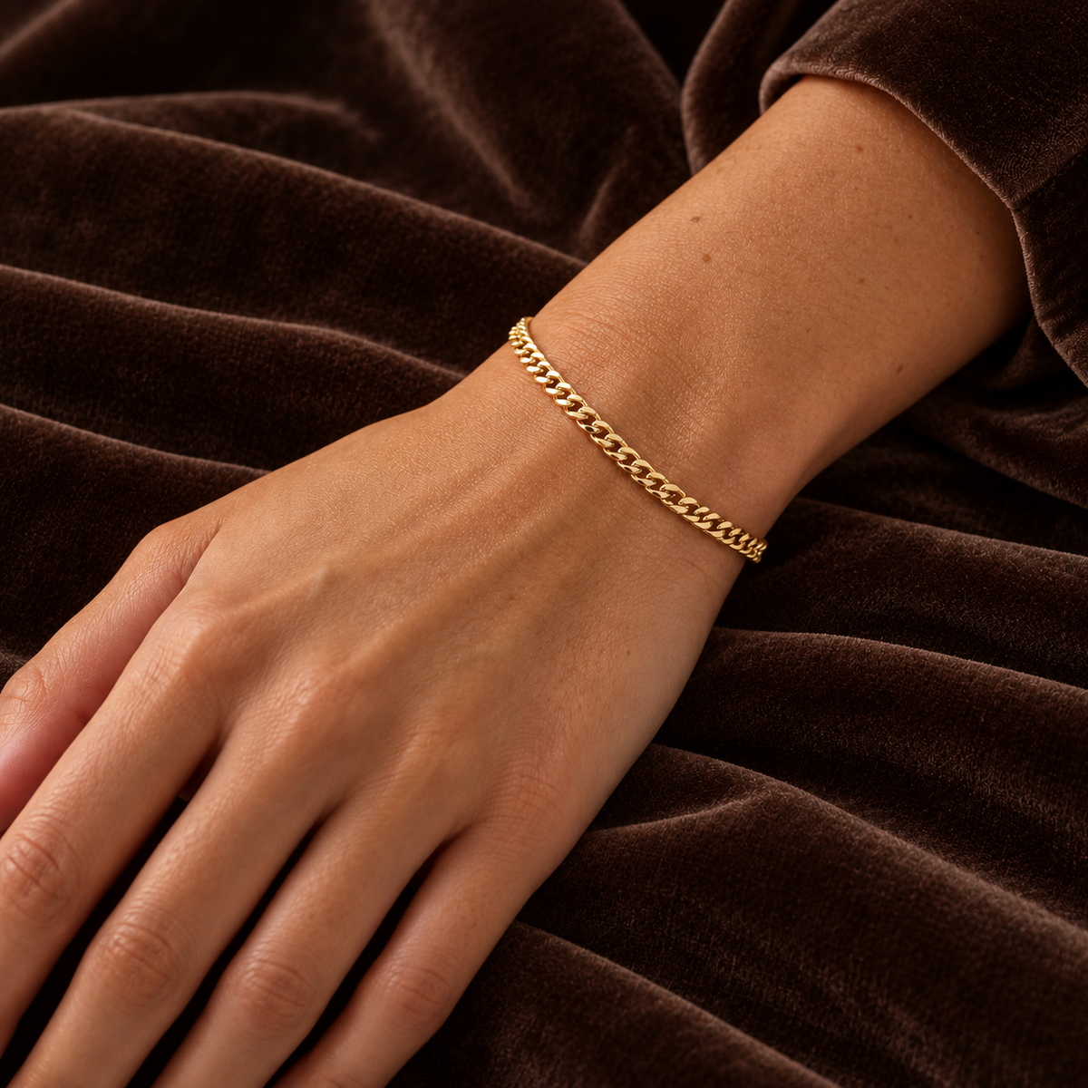 Gold Cuban Link Bracelet gedragen om een vrouwelijke pols op donkerbruin fluweel
