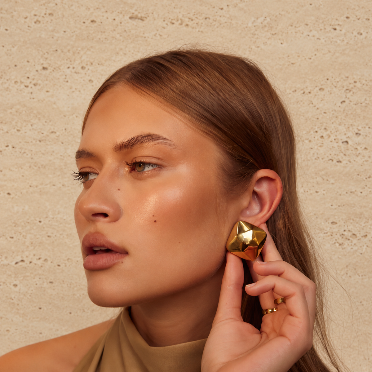 Gold Triangle Earrings gedragen tegen een lichtbeige natuurstenen achtergrond
