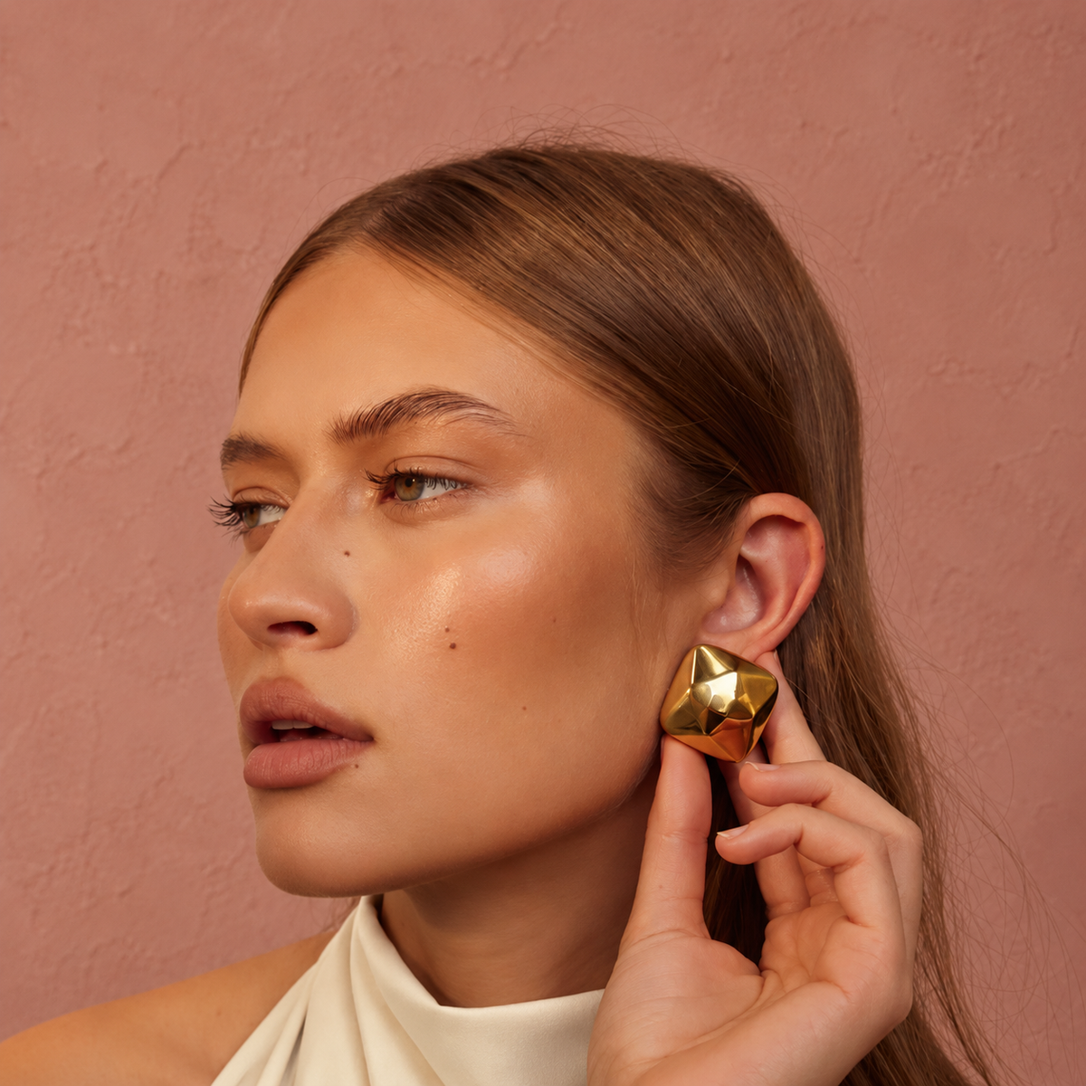 Gold Triangle Earrings gedragen door een vrouw tegen een warmroze achtergrond